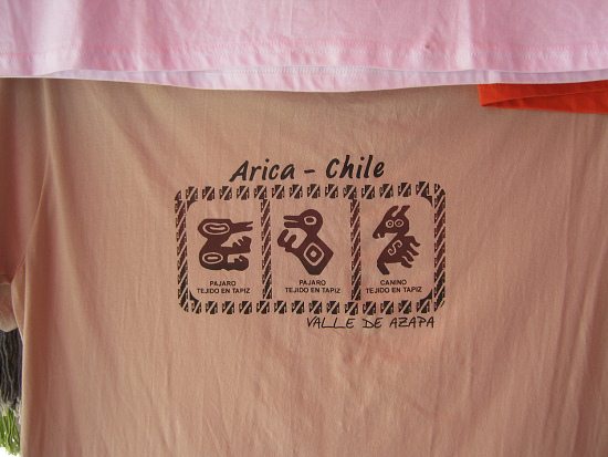 Braunes T-Shirt mit dem Design von
                                Geoglyphen, zwei V�geln und einem
                                hunde�hnlichen Tier ("canino")
                                mit der Angabe, dass diese Geoglyphen im
                                Azapa-Tal zu finden seien