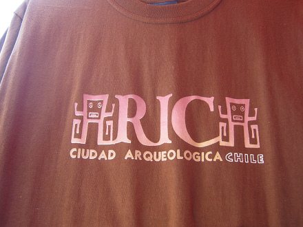 Braunes T-Shirt mit einem
                                Schriftzug "Arica" mit dem A
                                in Form einer menschen�hnlichen Figur
                                mit quadratischem Kopf mit rechteckigen
                                Lippen und Knopfaugen, und ohne Rumpf