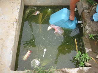Una habitante llenando el bid�n con el
                          agua fresca, y el bid�n mismo est� en el agua
                          sucia, primer plano